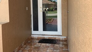 A door with a glass panel, leading to a patio area with a tiled floor and a small garden. - Relax at Key Largo (Key Largo)