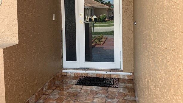 A door with a glass panel, leading to a patio area with a tiled floor and a small garden.
