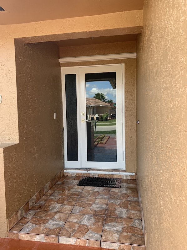 A door with a glass panel, leading to a patio area with a tiled floor and a small garden.
