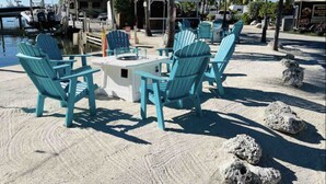 A beachside seating area with turquoise Adirondack chairs and a small table, surrounded by sand and palm trees. - Relax at Key Largo (Key Largo)