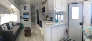 A compact RV interior with a kitchenette, a living area with a sofa, and a small dining table.