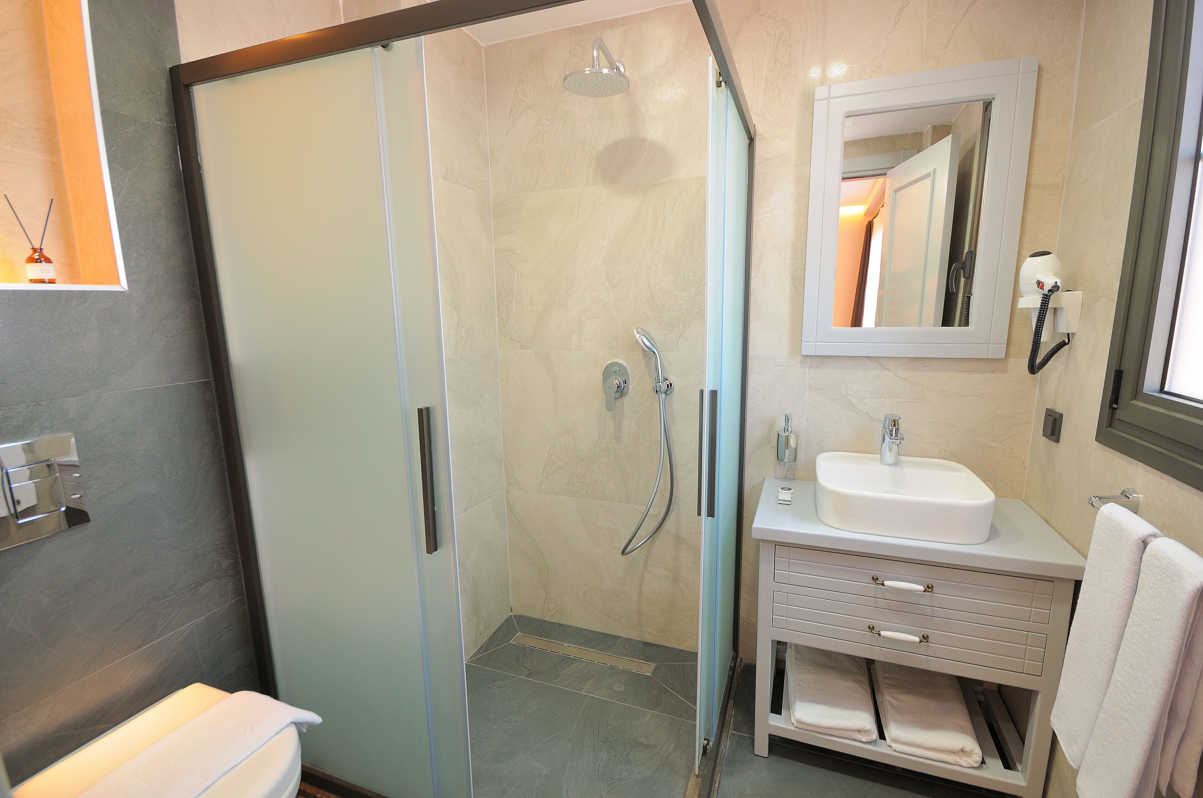 Un bany modern amb plat de dutxa envoltat de vidre, un lavabo blanc i un mirall a sobre.