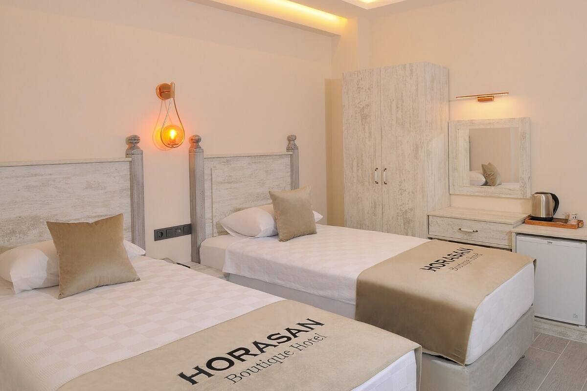 A hotel room with two beds, a wardrobe, a mirror, and a bedside table with a kettle.
