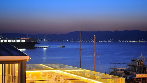 A dining area with tables and chairs, a view of the sea, and a ship in the background. - Horasan Hotel (Cesme)