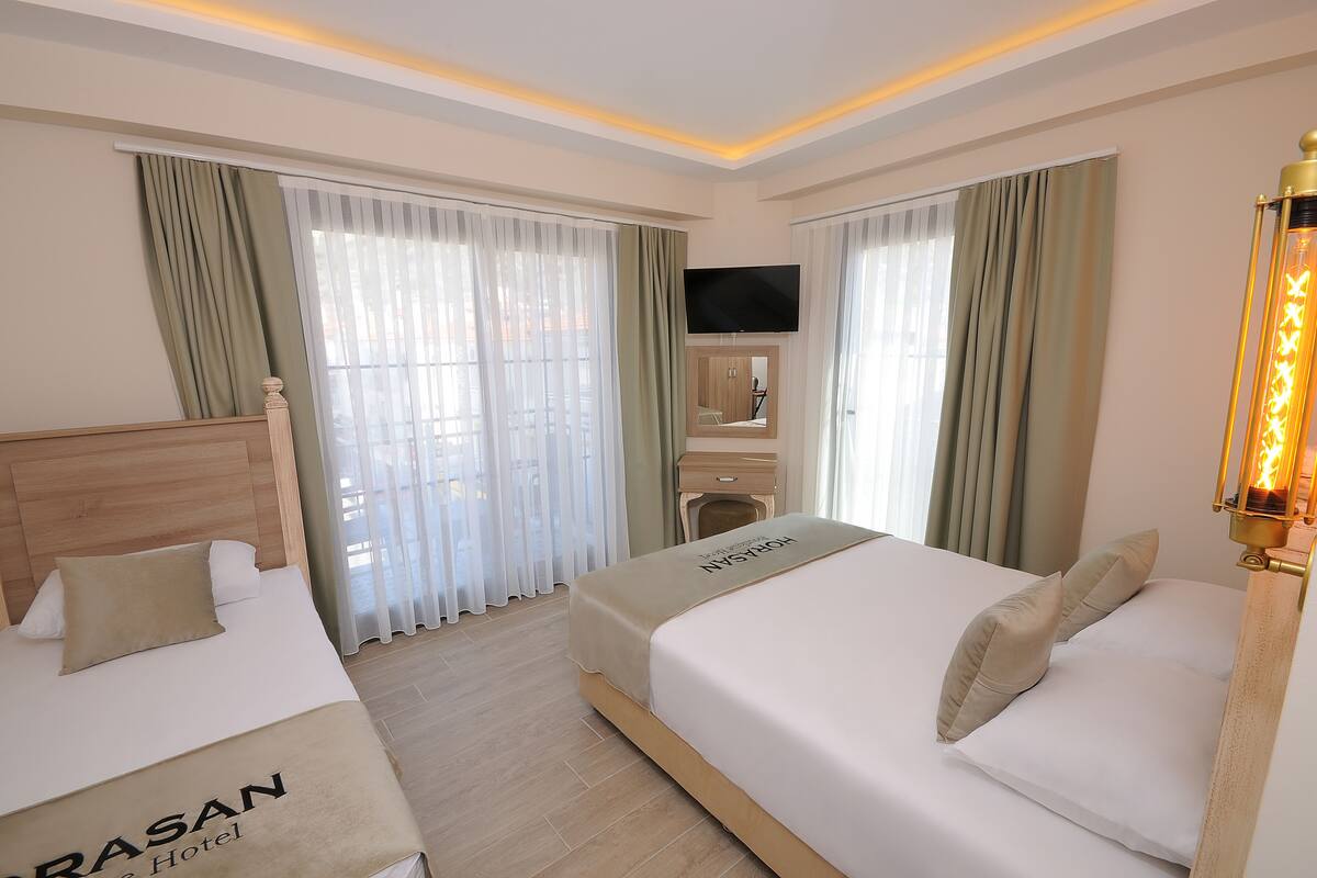 A hotel room with two beds, a flat-screen TV, a wooden headboard, and a bedside table with a lamp.