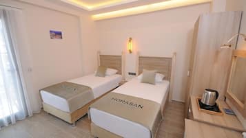 A hotel room with two beds, a wooden wardrobe, a bedside table with a kettle, and a small picture on the wall.