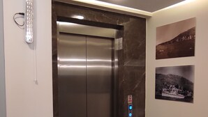 A modern elevator with a control panel, marble flooring, and wall-mounted artwork. - Horasan Hotel (Cesme)