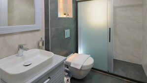 A modern bathroom with a white sink, a toilet, and a glass shower enclosure. - Horasan Hotel (Cesme)