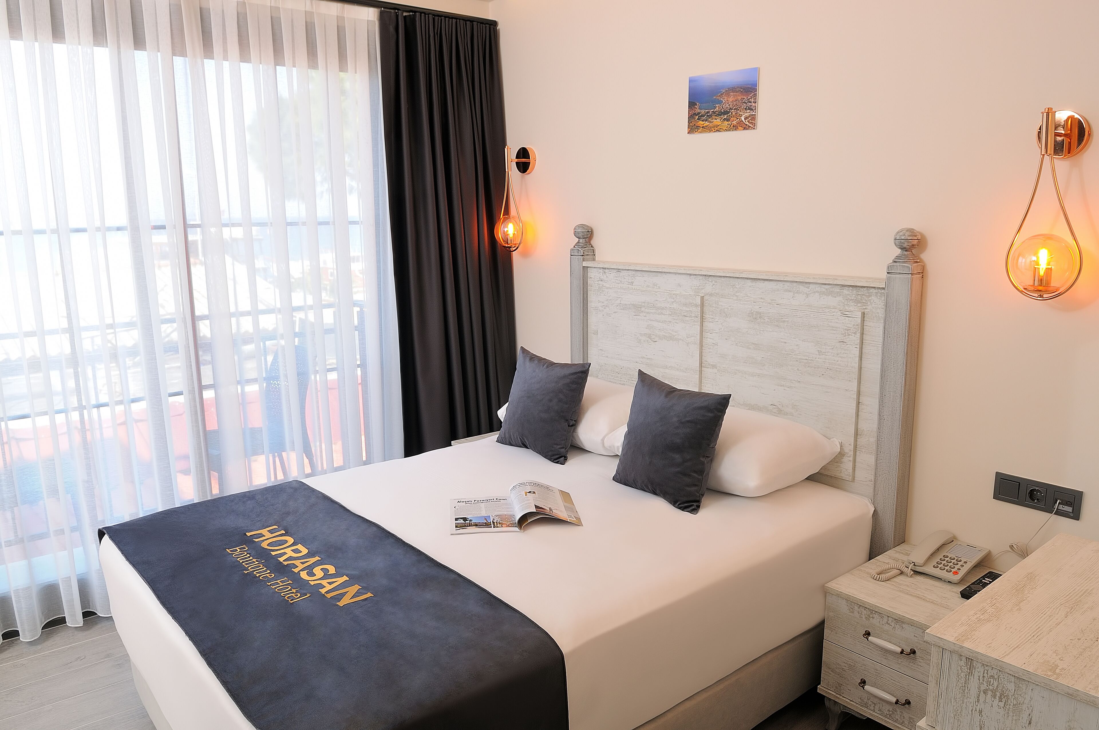Una habitación de hotel con una cama, una mesita de noche con teléfono y una ventana con cortinas.
