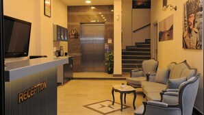 A hotel reception area with a reception desk, seating, a staircase, and a TV screen. - Horasan Hotel (Cesme)