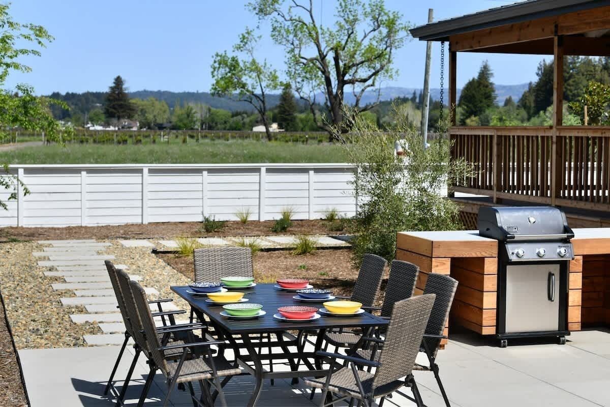 An outdoor patio with a table set for dining, surrounded by chairs, and a barbecue grill.