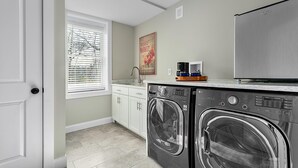 Une petite buanderie équipée d’un lave-linge et d’un sèche-linge, d’une machine à café et d’une fenêtre avec des stores.