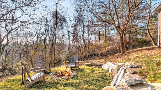 Un foyer extérieur entouré de deux fauteuils Adirondack, le tout délimité par un muret en pierre et bordé d’une pelouse avec des arbres en arrière-plan.