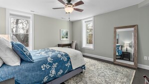 Une chambre à coucher avec un lit, un ventilateur de plafond, un grand miroir et des fenêtres.