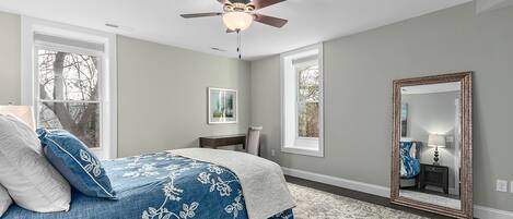 A bedroom with a bed, a ceiling fan, a large mirror, and windows.