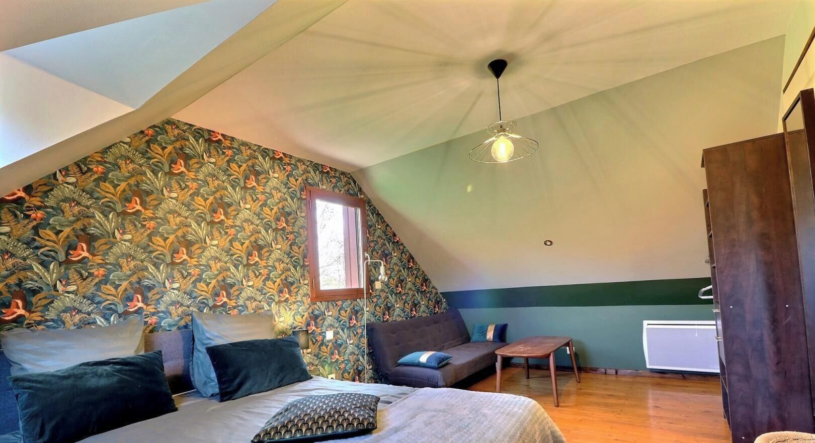 Ein Schlafzimmer mit schrägem Dach, einem Bett, einer Couch, einem kleinen Tisch und einer Heizung.