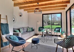 A modern interior with a grey sofa, green chairs, a patterned rug, and a large sliding glass door leading to a garden.