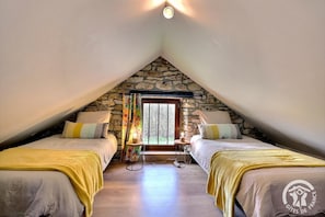 Une chambre avec deux lits, un mur en pierre, une fenêtre et une petite table avec une lampe.
