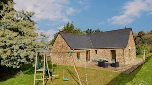A stone building with a sloped roof, a swing set, and outdoor seating.