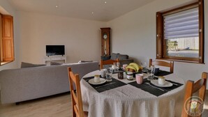 A dining area with a table set for four, a sofa in the background, and a clock on the wall.