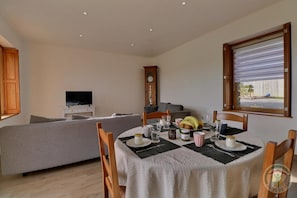 A dining area with a table set for four, a sofa in the background, and a clock on the wall.