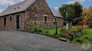 A stone building with a sloped roof, a gravel driveway, and a small garden with plants and flowers.