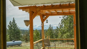 Eine Holzterrasse mit Stuhl und hängendem Korb, mit Blick auf eine gebirgige Landschaft.
