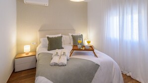Ein ordentlich bezogenes Bett mit grauer Decke, zwei Kissen und einem Tablett mit Orangensaftgläsern und einer Tasse.