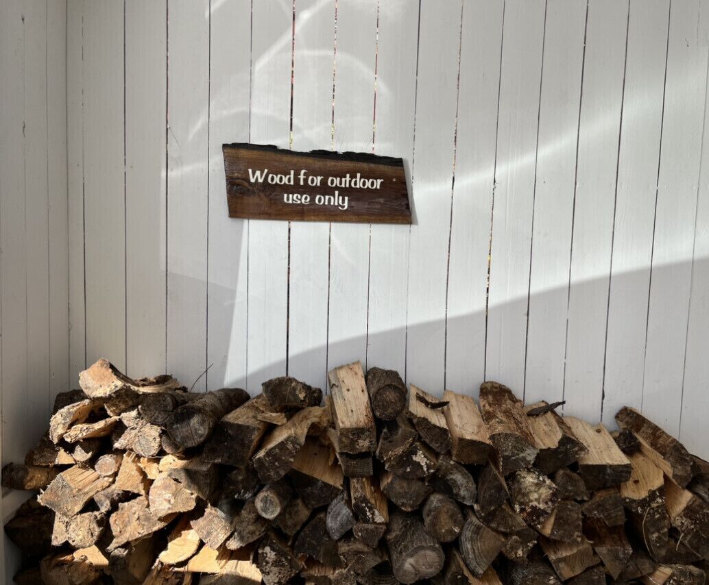 A stack of firewood against a white wall with a sign that reads "Wood for outdoor use only."