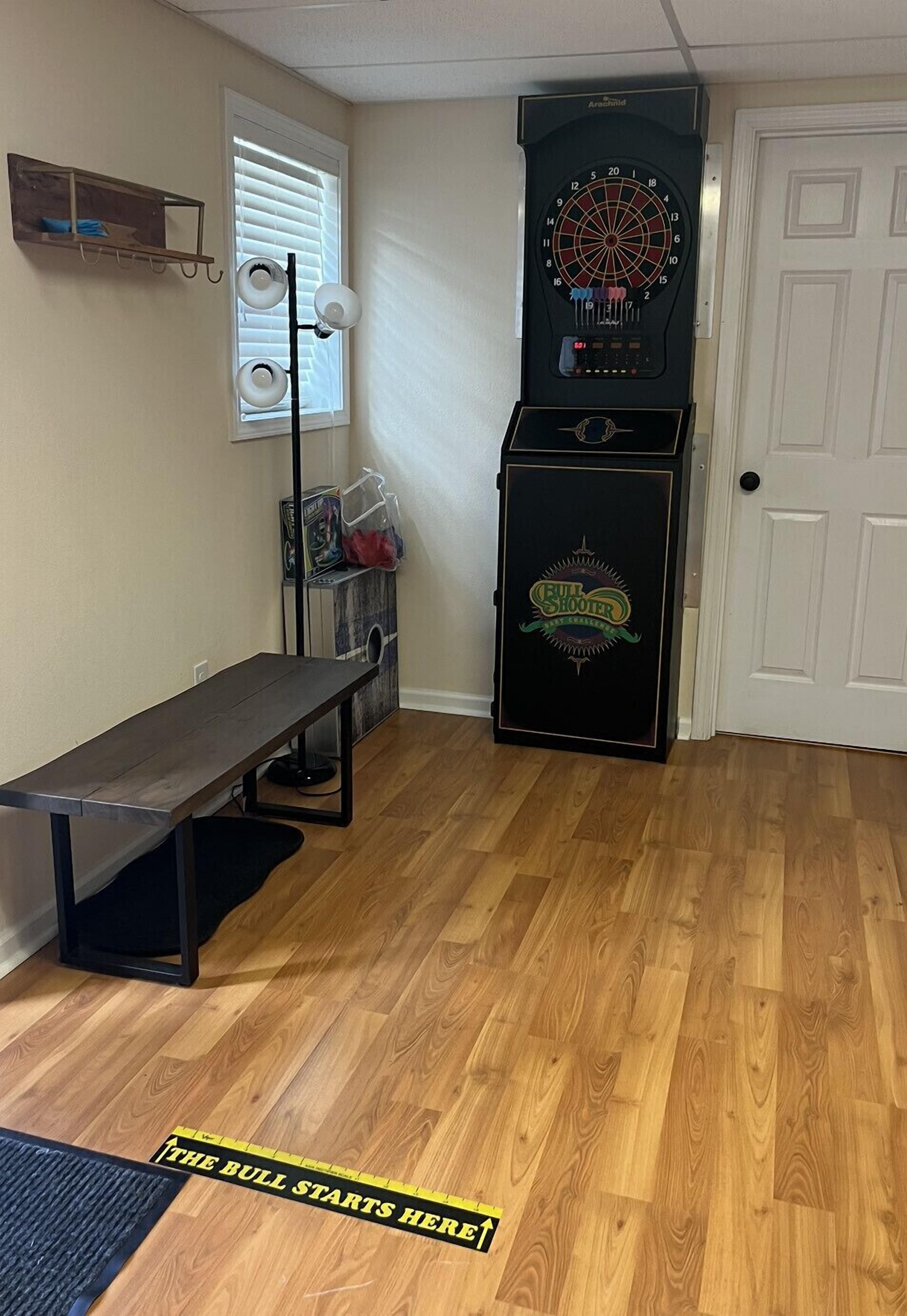 A room with a dartboard, a small table, a bench, and a door.