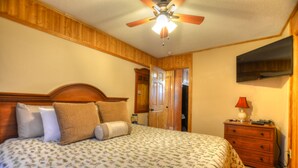 Quarto com cama, cabeceira de madeira, ventilador de teto, mesa de cabeceira com abajur e guarda-roupa.