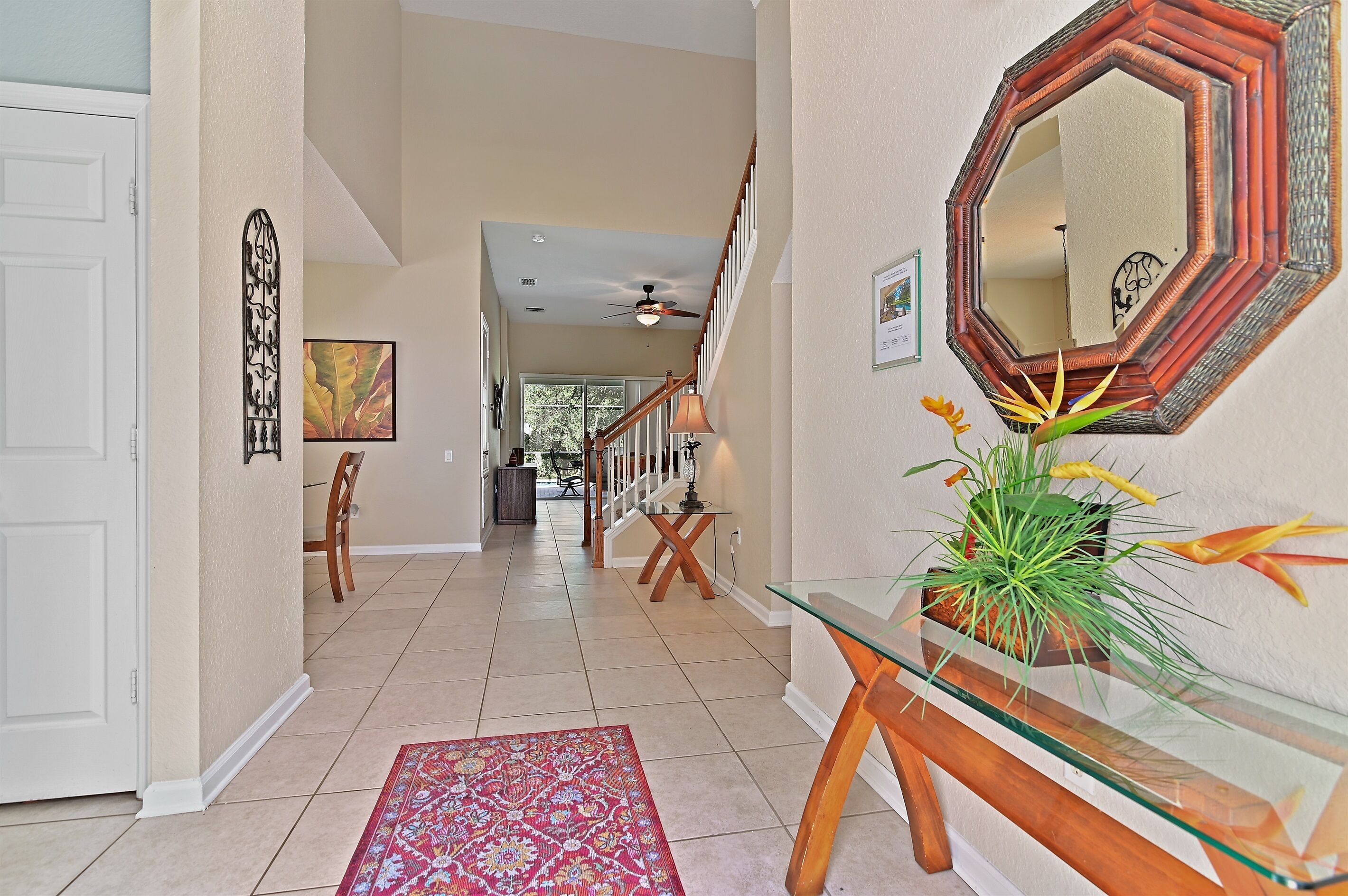 A hallway with a glass table, a potted plant, and a mirror on the wall.
