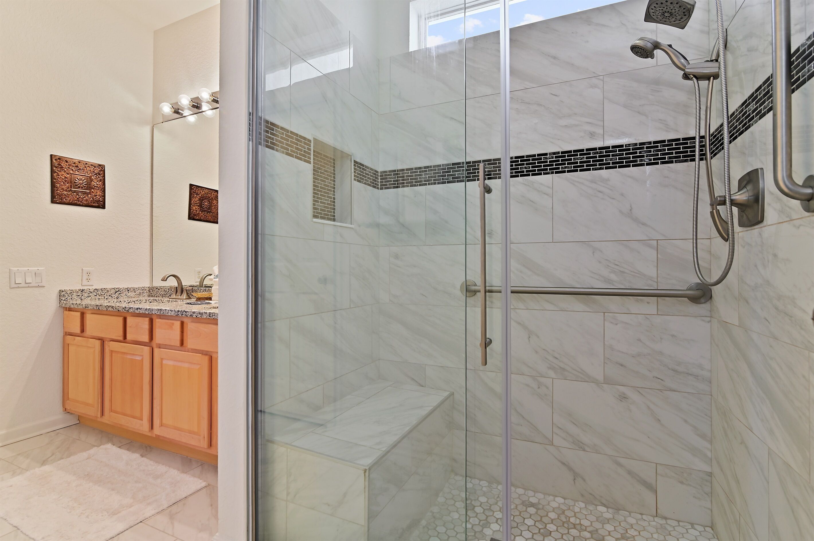 A bathroom with a glass-enclosed shower, marble tiles, wooden cabinets, and a small window.