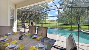 Un patio couvert avec vue sur la piscine, un espace salon extérieur et une table dressée pour les repas.