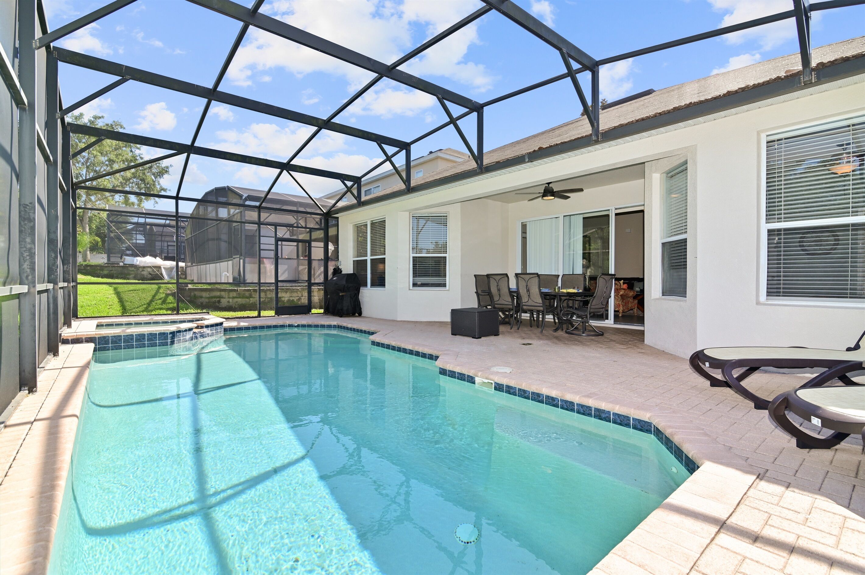 Ein Schwimmbad mit Glasveranda, Terrassenmöbeln und Blick auf die Nachbarschaft.