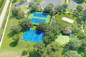 An aerial view of a tennis court complex surrounded by trees and a parking area.