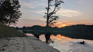 A sandy beach with footprints leading to calm water, a tree in the foreground, and a sunset in the background.