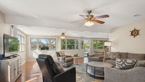 A spacious living room with a large window, a ceiling fan, and a television.