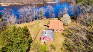 A red barn with a sloped roof, surrounded by trees and a body of water.