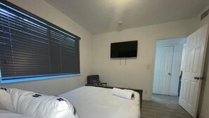 Habitación de hotel con una cama grande, un televisor de pantalla plana montado en la pared y una puerta que da a otra habitación.