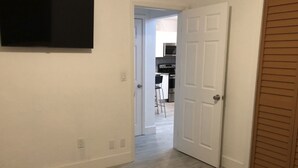 Un dormitorio con cama, una puerta blanca y vistas a una zona de cocina.