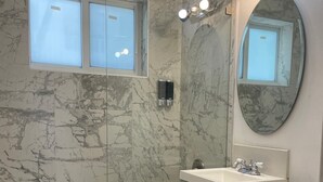 Un baño con pared de mármol, una bañera, un inodoro, un lavabo y un espejo.