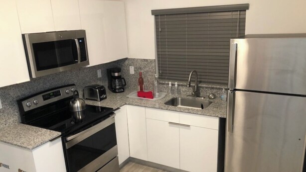 Una cocina moderna con electrodomésticos de acero inoxidable, armarios blancos y una encimera de granito.