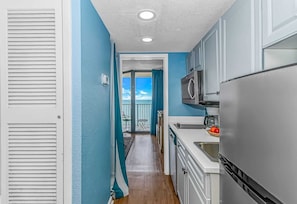A kitchen with a refrigerator, microwave, and a view to a balcony.