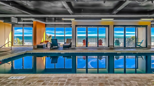 Indendørs pool med havudsigt, loungeområde med stole og en poolbar.