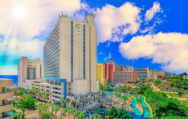 A hotel with a prominent tower, a pool area, and a view of the surrounding cityscape.
