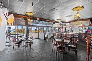 A restaurant interior with a beach-themed decor, including a sign that reads 'BEACHFRONT Kitchen & Bar,' and a view of palm trees outside.
