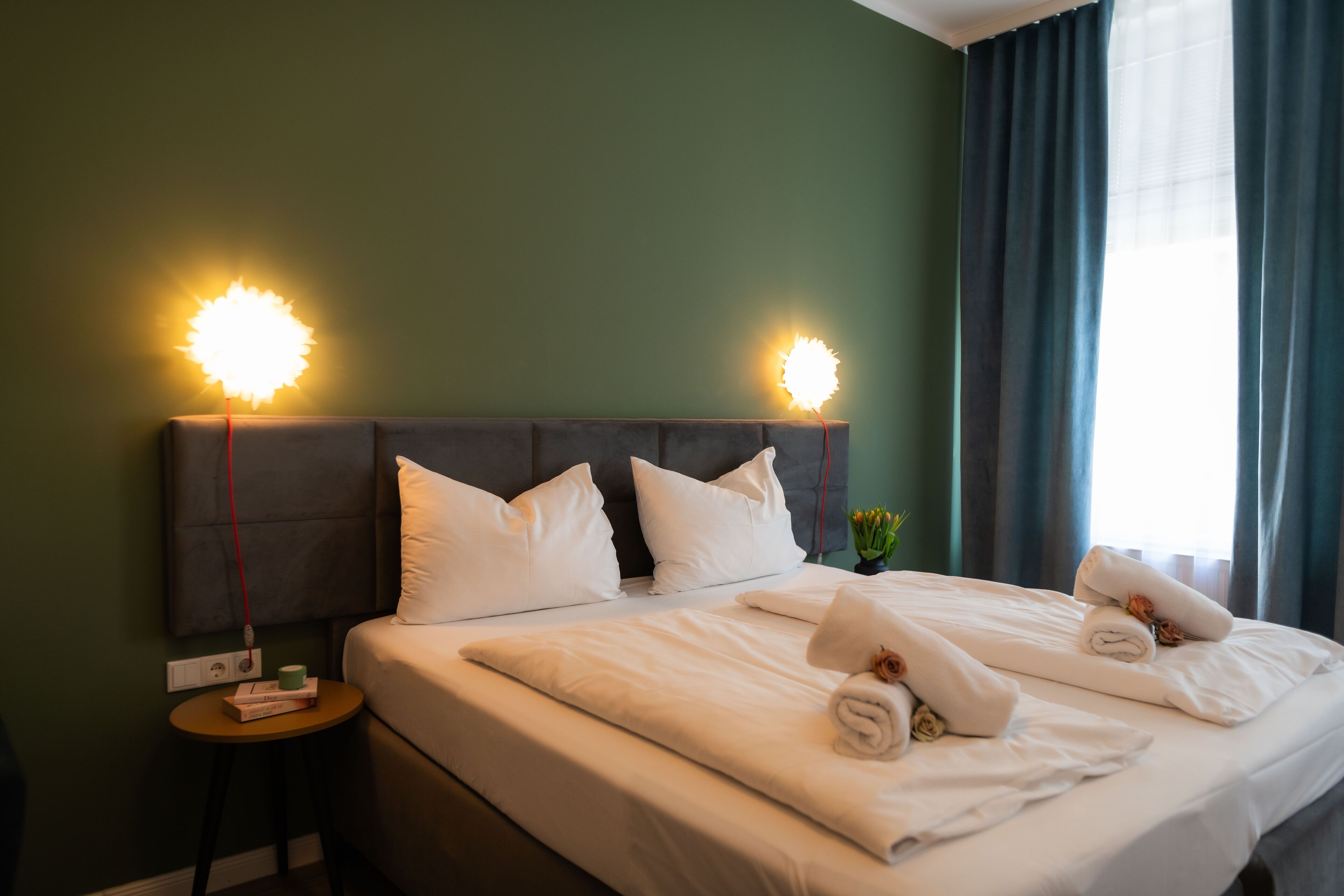 A hotel room with a bed, pillows, a nightstand, and two wall-mounted lamps.