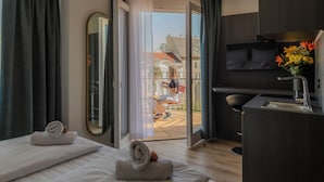 Een moderne hotelkamer met een bed, een bureau, een televisie en een balkon met uitzicht op gebouwen.