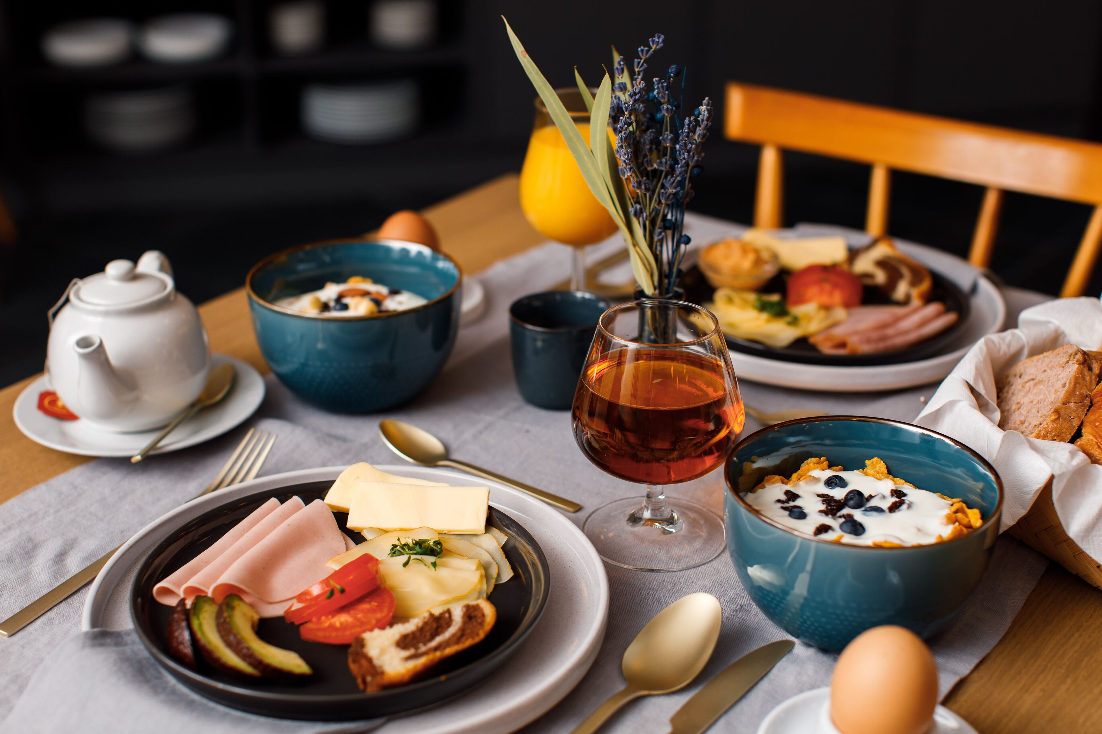 Ein Frühstückstisch mit Tellern voller Speisen, einem Teekessel und einem Glas Saft.